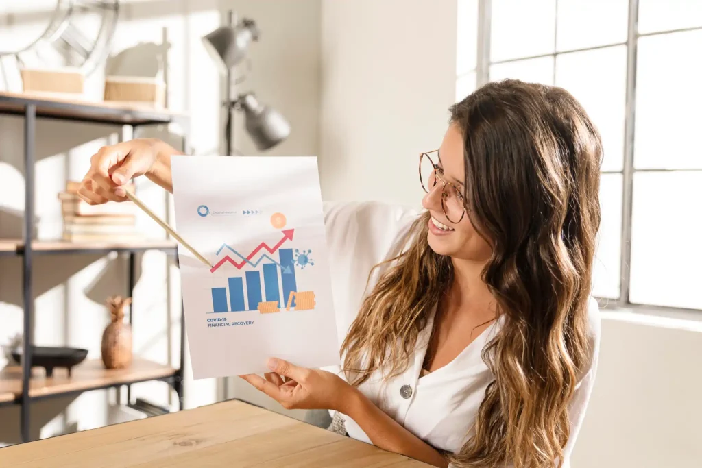 Marketing Local | Estrategias para Negocios Locales 3 Mujer profesional señalando un gráfico con barras y flechas ascendentes. Simboliza la recuperación financiera y el crecimiento constante de las ventas.
