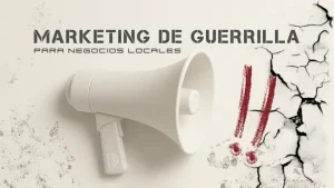 Imagen en tonos neutros que muestra un megáfono blanco apuntando hacia la derecha. A su lado, la pared aparece resquebrajada y con marcas rojas de exclamación dibujadas a mano, simbolizando el impacto y la disrupción del marketing de guerrilla. En la parte superior se lee “Marketing de guerrilla para negocios locales” con tipografía estilo stencil.